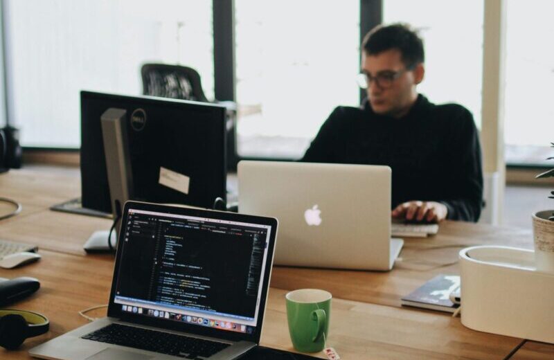 A web developer working on code in a modern office setting with multiple devices.